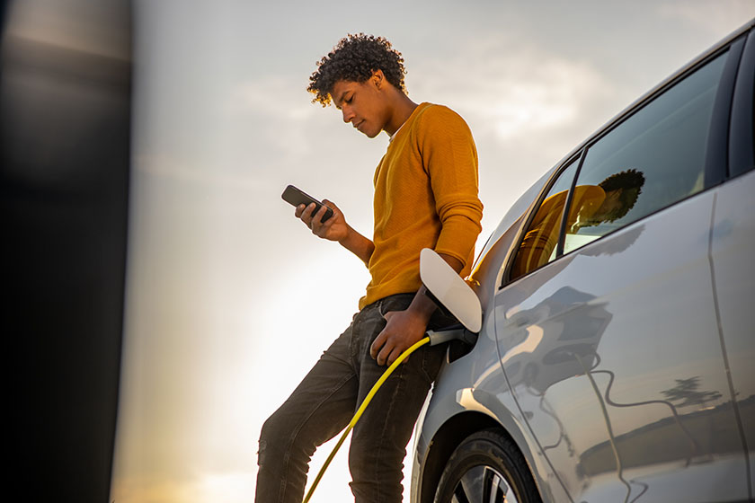 African american man using mobile phone while he is waiting for his electric car to be charged at charging station